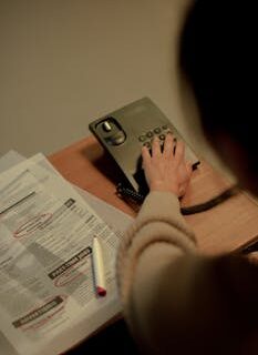 Woman using a phone to inquire about job postings, newspaper and pen on a table.