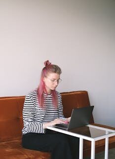 Young woman with pink hair working on a laptop at home, embodying the freelance lifestyle.